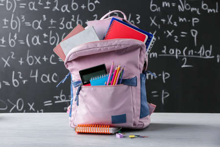 Stylish school backpack with stationery on table in classroomの写真素材