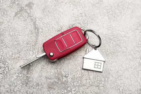 Red car key with house shape keychain on grunge background