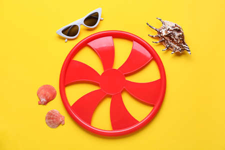 Flying disc, sunglasses and seashells on color background