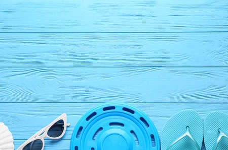 flying disk, sunglasses and flip-flops on color wooden background
