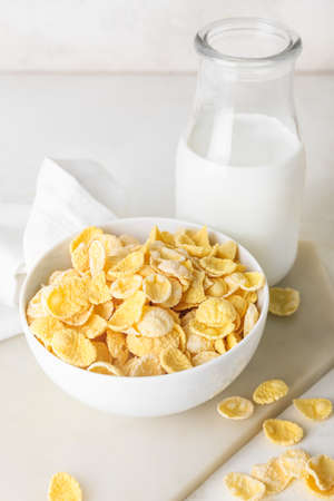 Bowl with tasty cornflakes and bottle of milk on light background