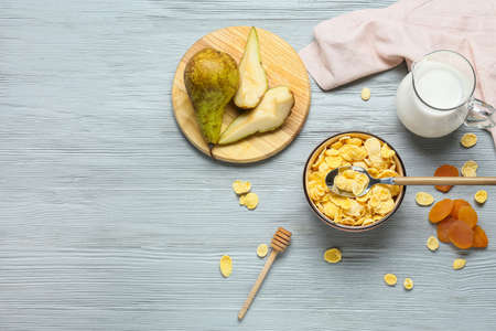 Composition with tasty cornflakes, fruits and jug of milk on gray wooden background