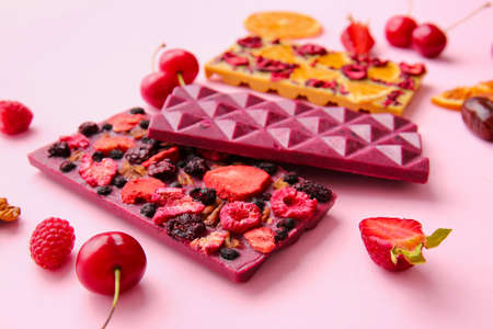 Handmade chocolate bars with fruits, berries and nuts on color background, closeup