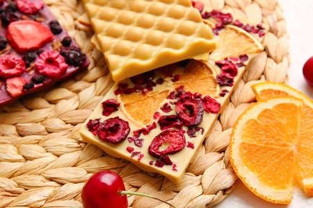 Handmade chocolate bars with fruits, berries and nuts on wicker mat, closeupの写真素材