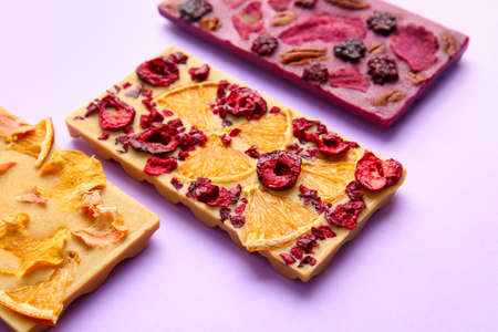 Handmade chocolate bars with fruits, berries and nuts on color background, closeup