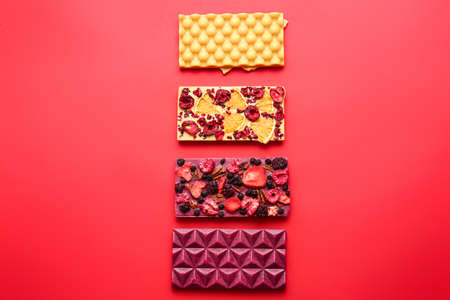 Handmade chocolate bars with fruits, berries and nuts on color background