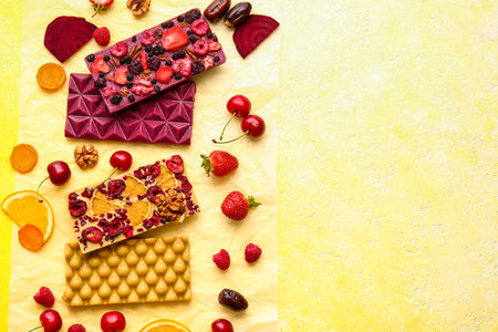 Handmade chocolate bars with fruits, berries and nuts on color background
