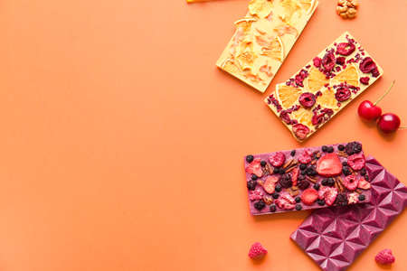 Handmade chocolate bars with fruits, berries and nuts on color background