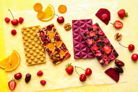 Handmade chocolate bars with fruits, berries and nuts on color background