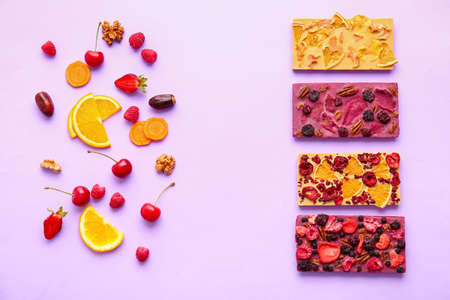 Handmade chocolate bars with fruits, berries and nuts on color background