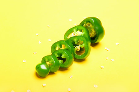 Slices of green jalapeno peppers on color background