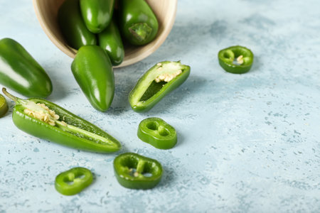 Bowl with cut green jalapeno peppers on color background, closeup