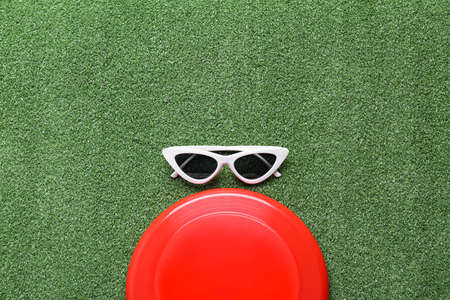 Flying disk and sunglasses on color background