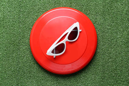 Flying disk and sunglasses on color background