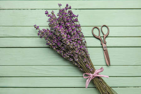 Bouquet of lavender flowers and scissors on color wooden background