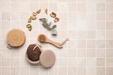 Different massage brushes and bath supplies on light tile background