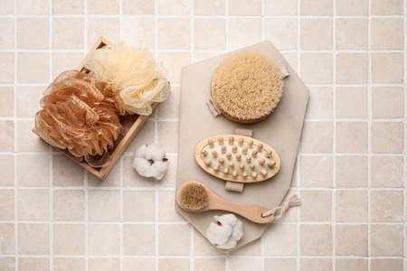 Different massage brushes and bath supplies on light tile background