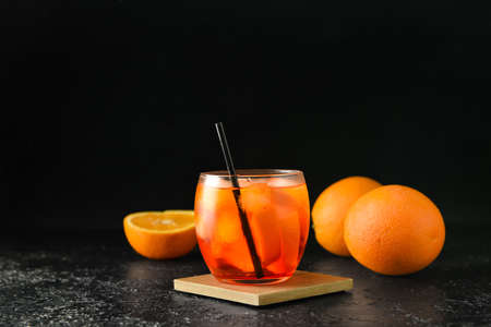 Glass of tasty aperol spritz cocktail and fresh oranges on dark background