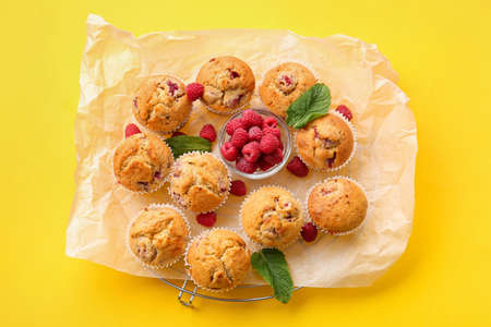 Parchment with tasty raspberry muffins on color background