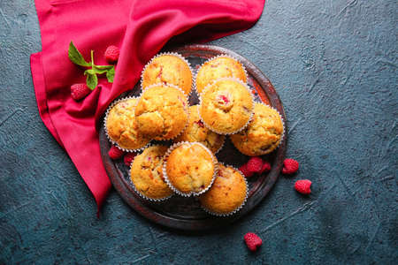 Plate with tasty raspberry muffins on color background