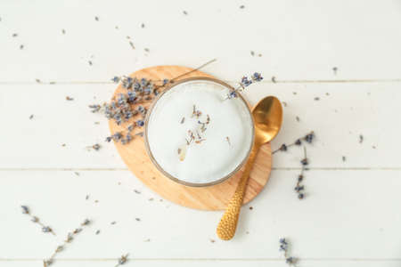 Glass of tasty lavender latte and flowers on light wooden background