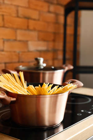 Copper cooking pot with raw spaghetti on stove in kitchen, closeup