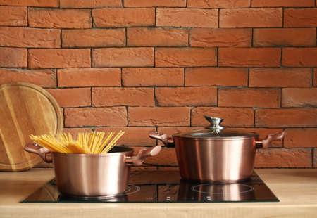 Copper cooking pots with raw spaghetti on stove in modern kitchen