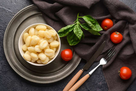 Bowl with tasty gnocchi and tomatoes on dark background