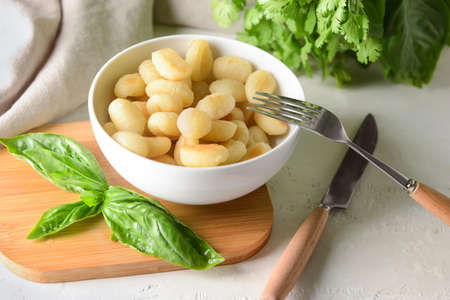 Bowl with tasty gnocchi on light background