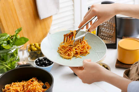 Woman preparing tasty Pasta Puttanesca at kitchen tableの写真素材