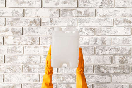 Male hands in rubber gloves holding canister near brick wall