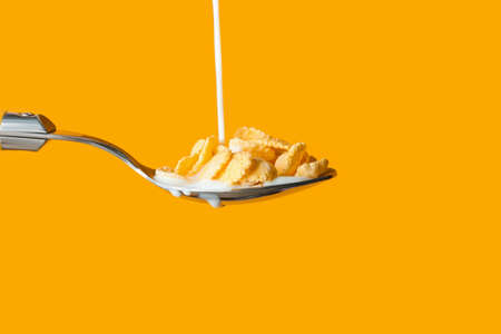 Pouring of milk into spoon with cornflakes on color background, closeup