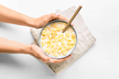Woman holding bowl of tasty cornflakes with milk on light wooden background