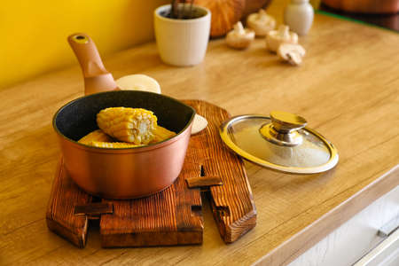 Sauce pan with corn cobs on wooden tableの写真素材