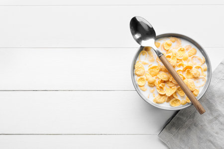Bowl of tasty cornflakes with milk and spoon on light wooden backgroundの写真素材
