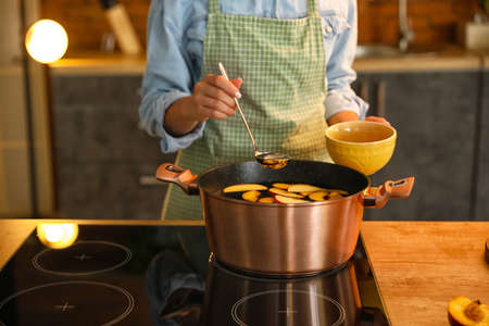 Woman pouring compote to cup in kitchen