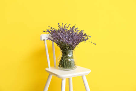 Vase with beautiful lavender flowers on chair against color backgroundの写真素材