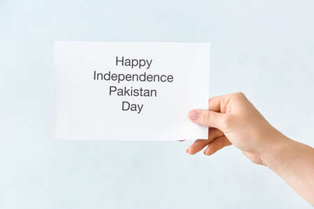 Female hand holding greeting card for Independence Day of Pakistan on light backgroundの写真素材