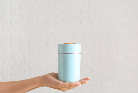 Hand with modern air humidifier on light background