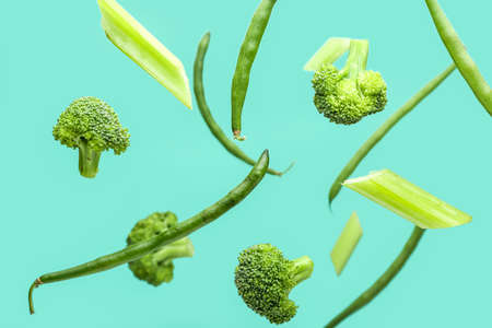 Flying green vegetables on color background