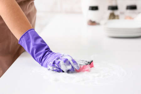 Woman cleaning table with sponge and foam in kitchenの写真素材