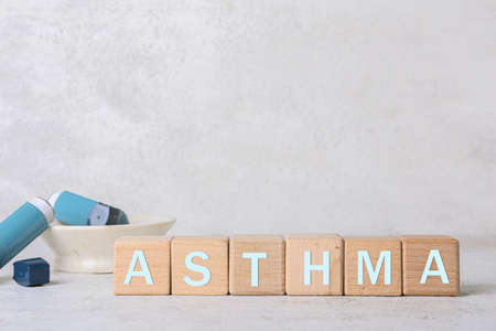 Word ASTHMA made of cubes and inhalers on table