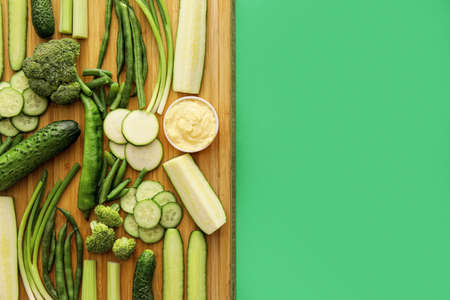 Board with different green vegetables and bowl with sauce on color backgroundの写真素材