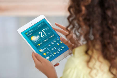 Young woman with tablet computer using weather forecast application at homeの写真素材
