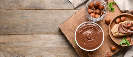 Bowl with tasty chocolate butter and hazelnuts on wooden background with space for text