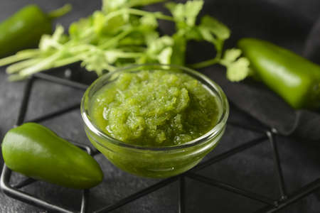 Bowl of Tomatillo Salsa Verde sauce and jalapeno pepper on dark background, closeupの写真素材