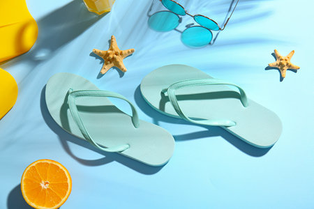 Stylish flip-flops and sunglasses on color background