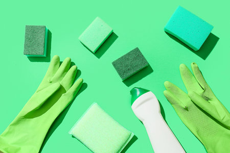 Green cleaning sponges, gloves and bottle of detergent on color backgroundの写真素材