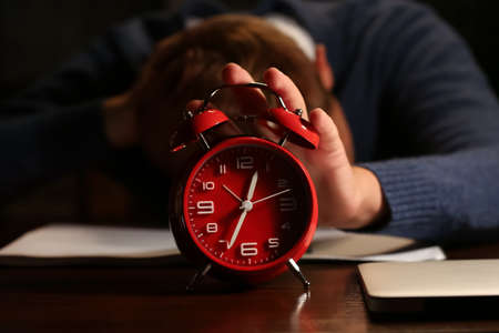 Sleeping young man with alarm clock in office at night, closeup