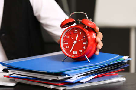 Young businessman with red alarm clock and folders sitting at table in office, closeupの写真素材
